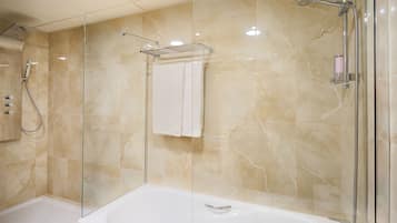Un baño moderno con ducha y bañera separados por vidrio, y pared con azulejos de mármol.