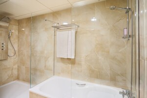 Un baño moderno con ducha y bañera separados por vidrio, y pared con azulejos de mármol.