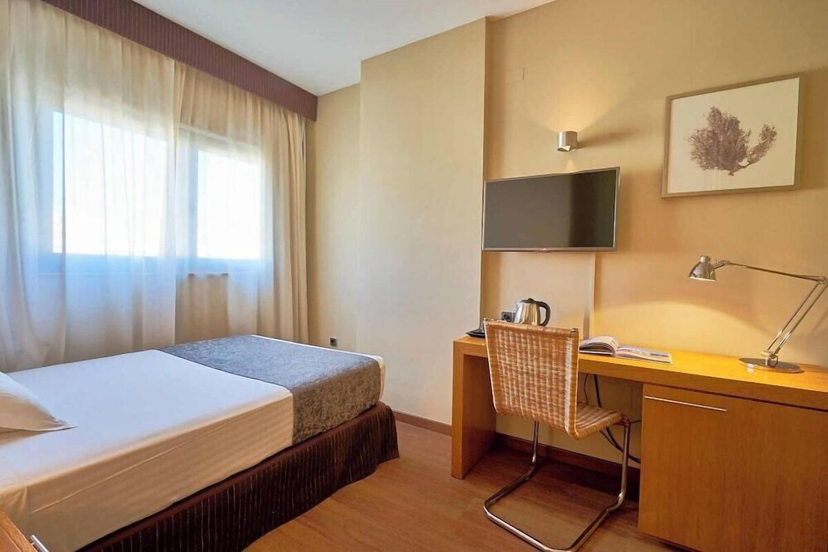 A hotel room with a bed, a desk, a chair, a TV, and a framed picture on the wall.