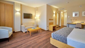 Una habitación de hotel con cama, sofá, escritorio, silla, una mesita y armario.