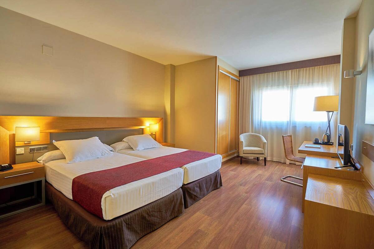 Una habitación de hotel con dos camas, un escritorio, una silla y un televisor.