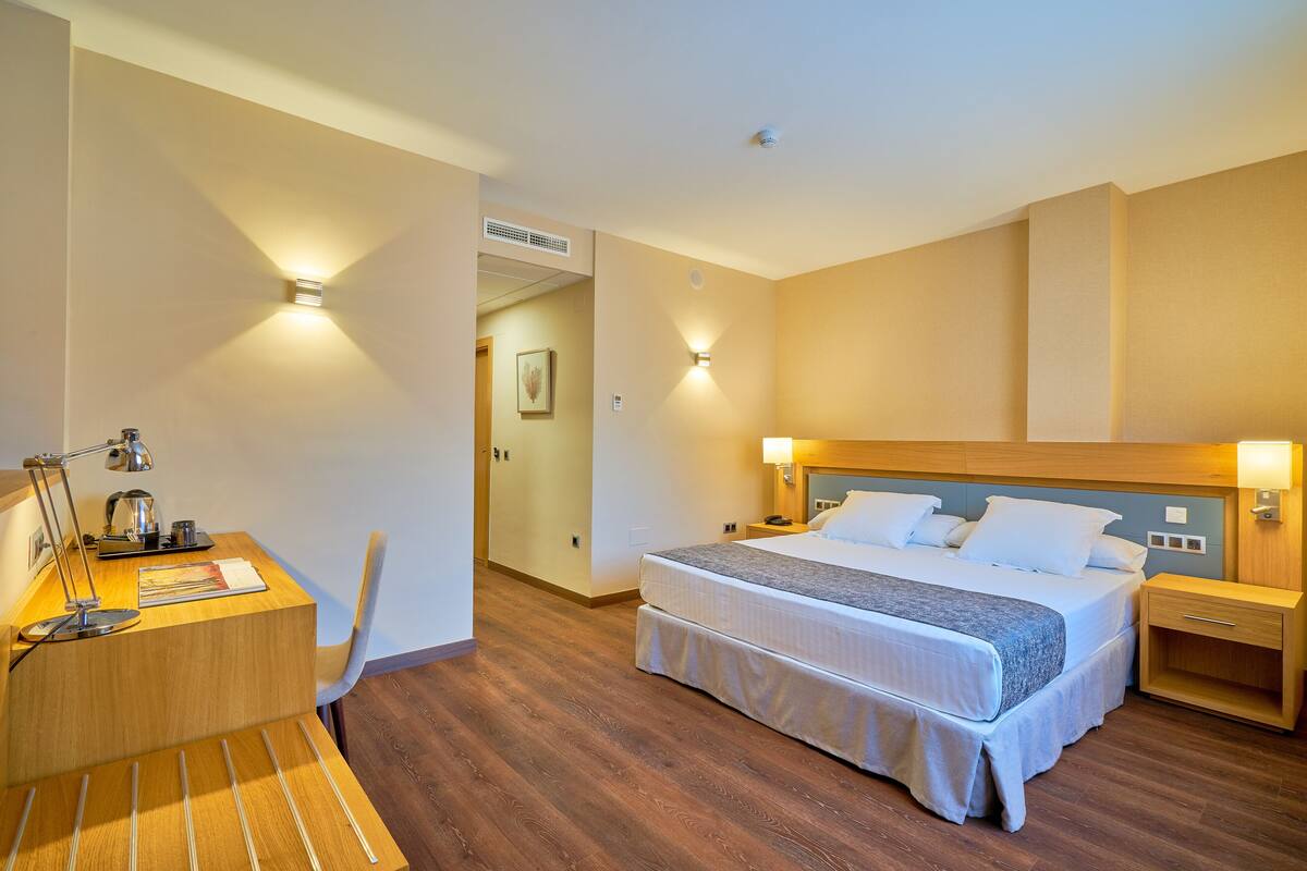 Una habitación de hotel con un escritorio de madera, una cama con ropa de cama blanca y dos lámparas de noche.