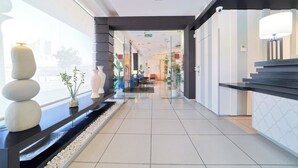 Un moderno vestíbulo de hotel con una recepción, un área de estar y vistas de la ciudad a través de amplias ventanas.