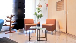 Un salón moderno con dos sillones naranjas, una mesa de centro de vidrio, una lámpara de pie, una planta en maceta y una escultura de madera con forma de árbol.