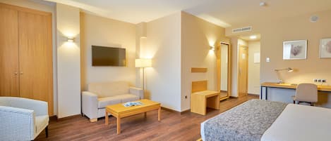 Habitación de hotel con cama, sofá, escritorio, silla, armario de madera y televisor.