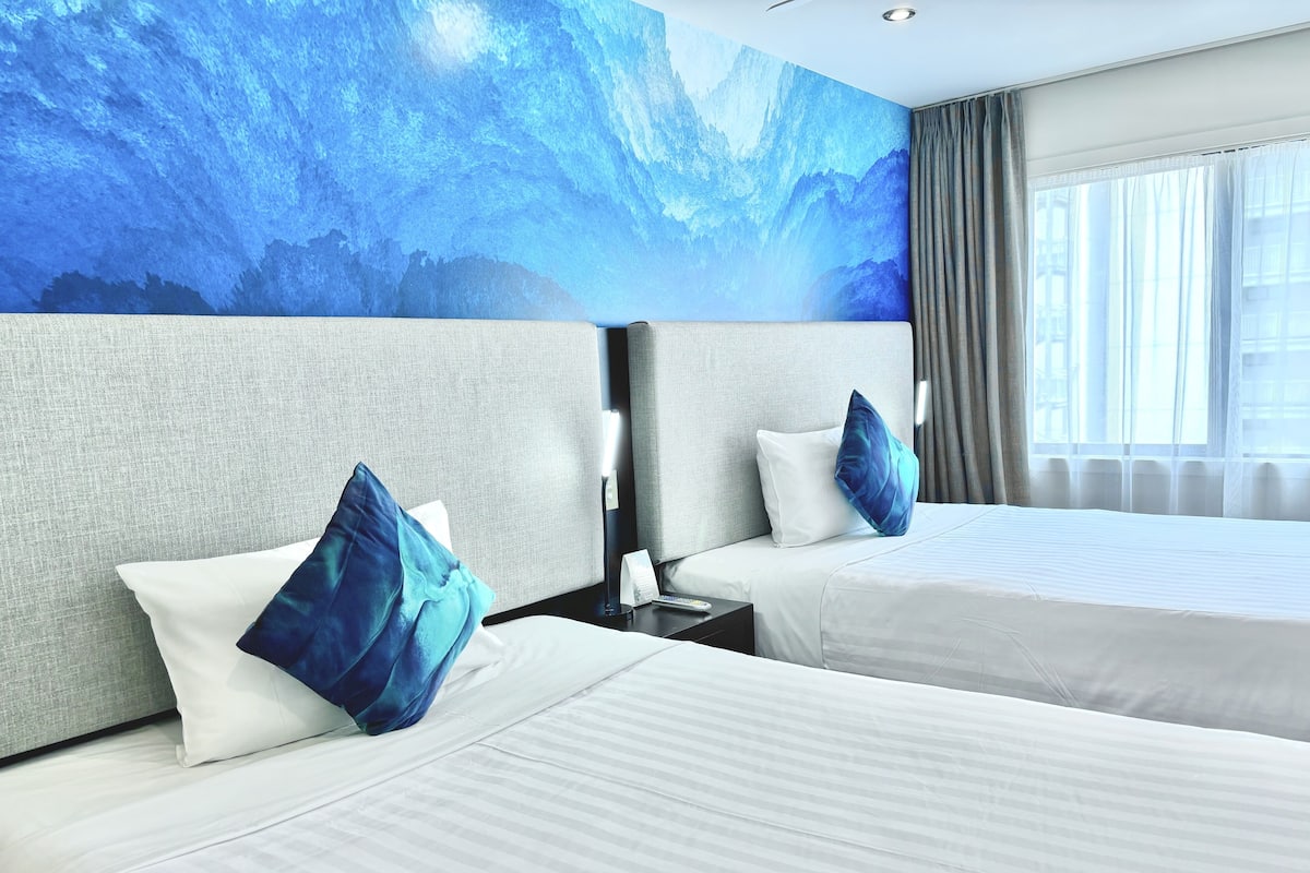 Une chambre d’hôtel avec deux lits, une grande fresque murale et une fenêtre avec des rideaux.