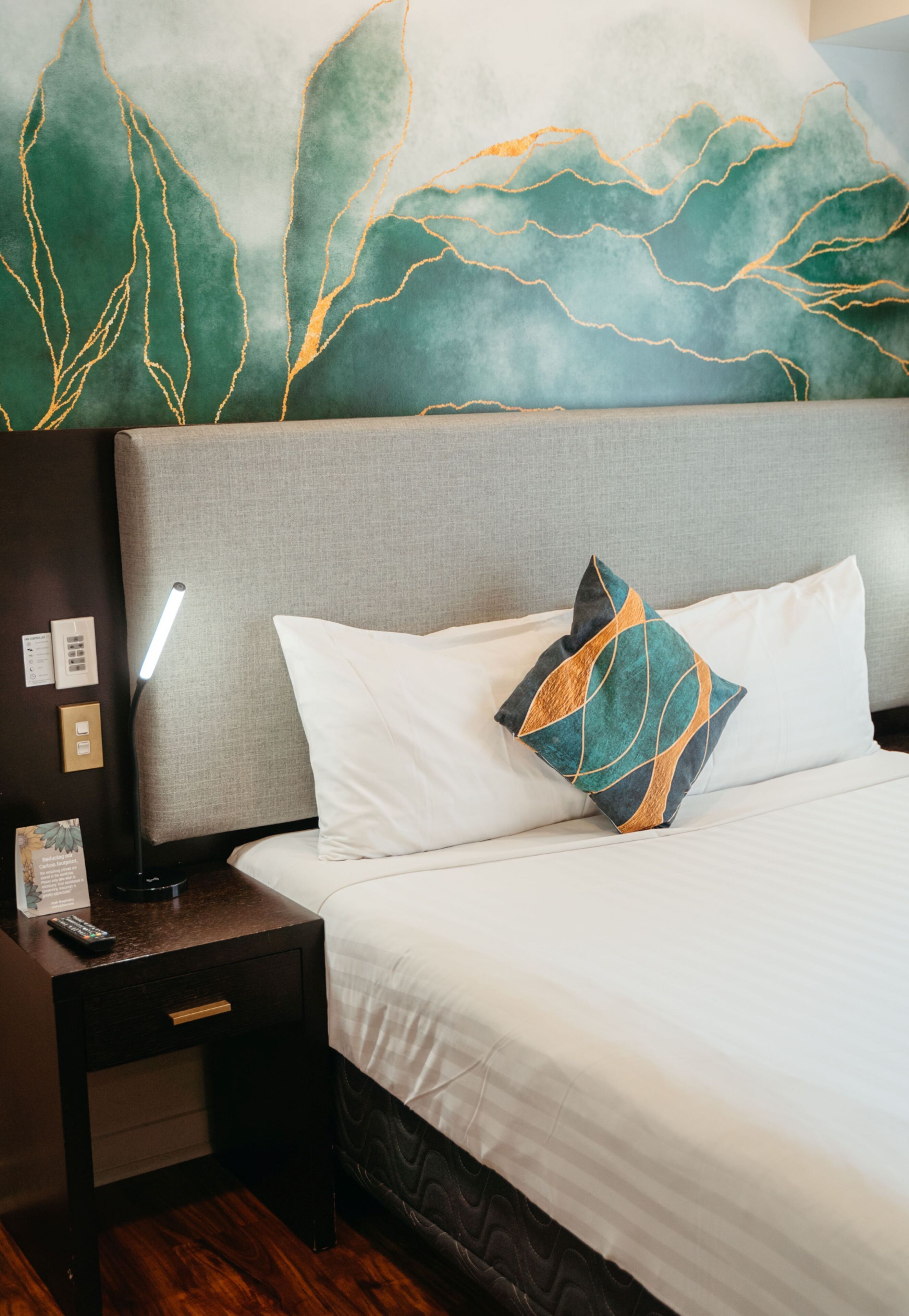 A hotel room with a bed, a nightstand, a lamp, and a wall with a leaf pattern.