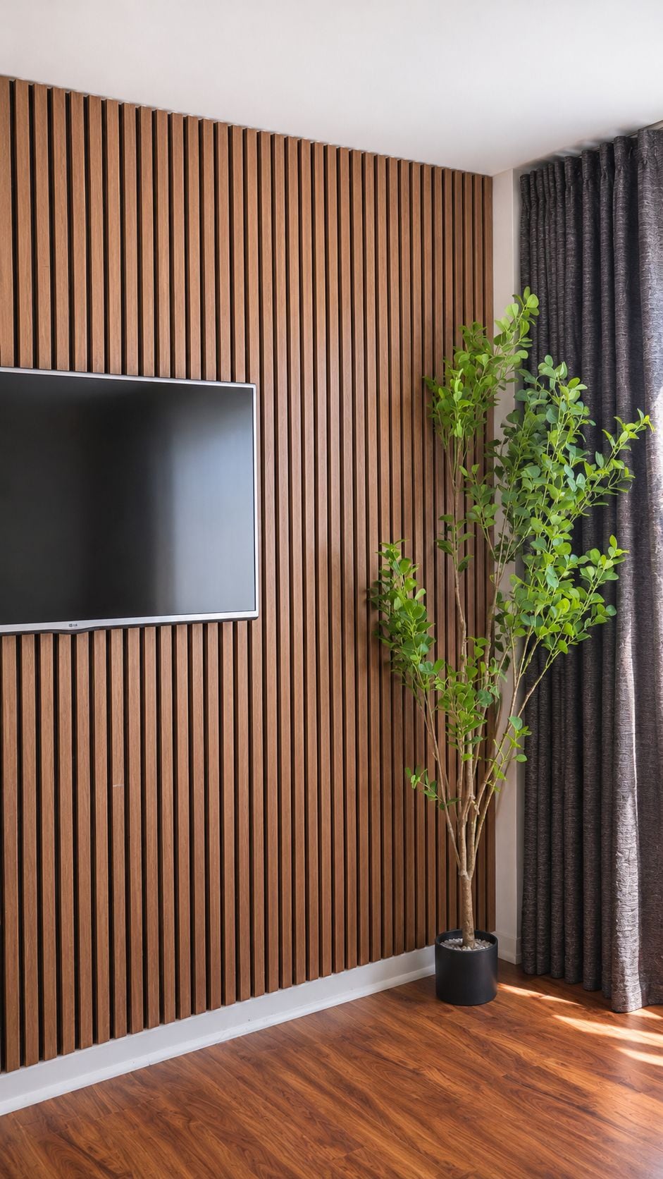 A room with a wooden slatted wall, a flat-screen TV mounted on it, and a potted plant.