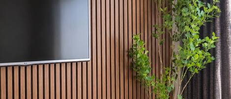 A room with a wooden slatted wall, a flat-screen TV mounted on it, and a potted plant.