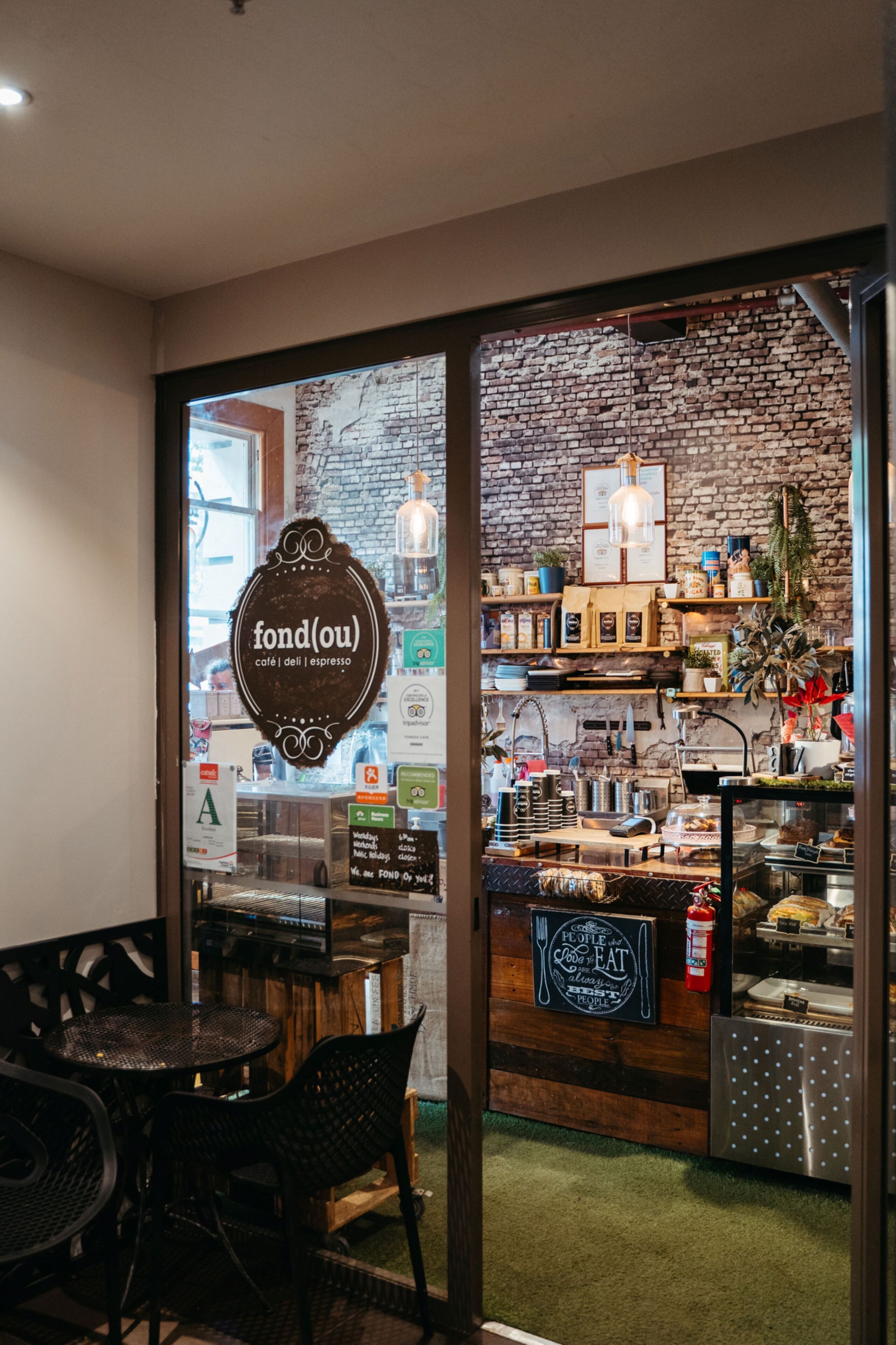 A café interior with a brick wall, wooden shelves, and a chalkboard menu.