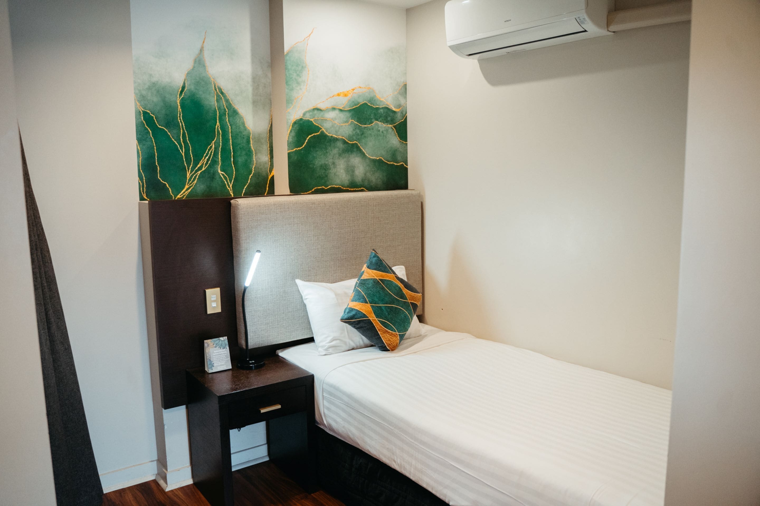 A hotel room with a bed, nightstand, lamp, and artwork on the wall.