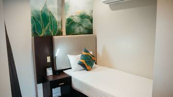 A hotel room with a bed, nightstand, lamp, and artwork on the wall.