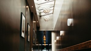 A modern hotel corridor with a reflective floor, framed artwork on the walls, and a ceiling with a unique light fixture. - Auckland City Hotel (Auckland)