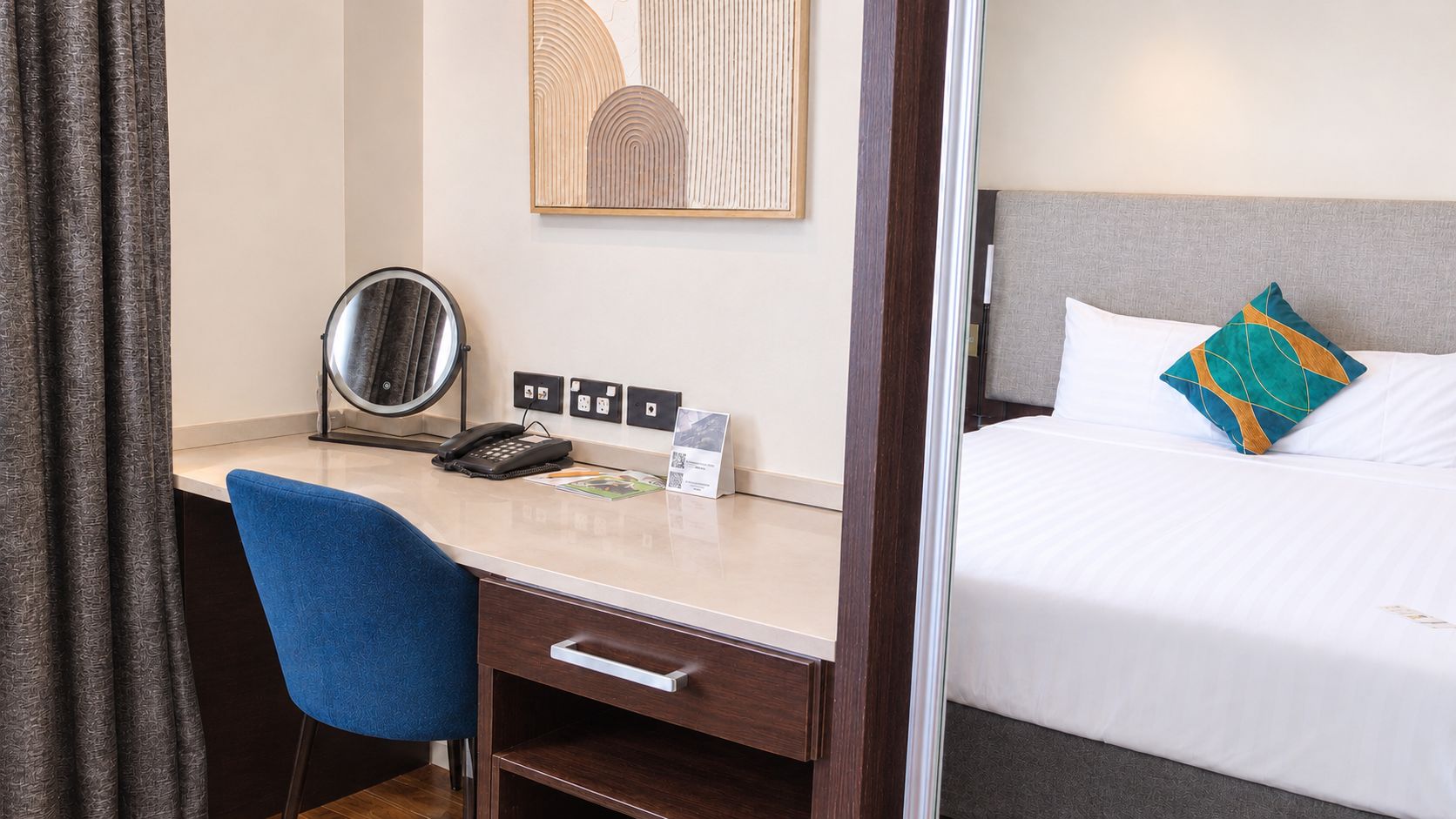 Une chambre d’hôtel comprenant un lit, un bureau avec un téléphone, une chaise et un miroir fixé au mur.