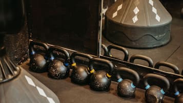 A row of black kettlebells with blue and yellow markings, arranged on a dark floor.