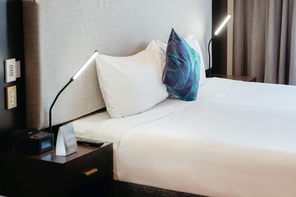 Une chambre d’hôtel avec un grand lit, une table de chevet avec une lampe, une télécommande et un téléphone fixé au mur.