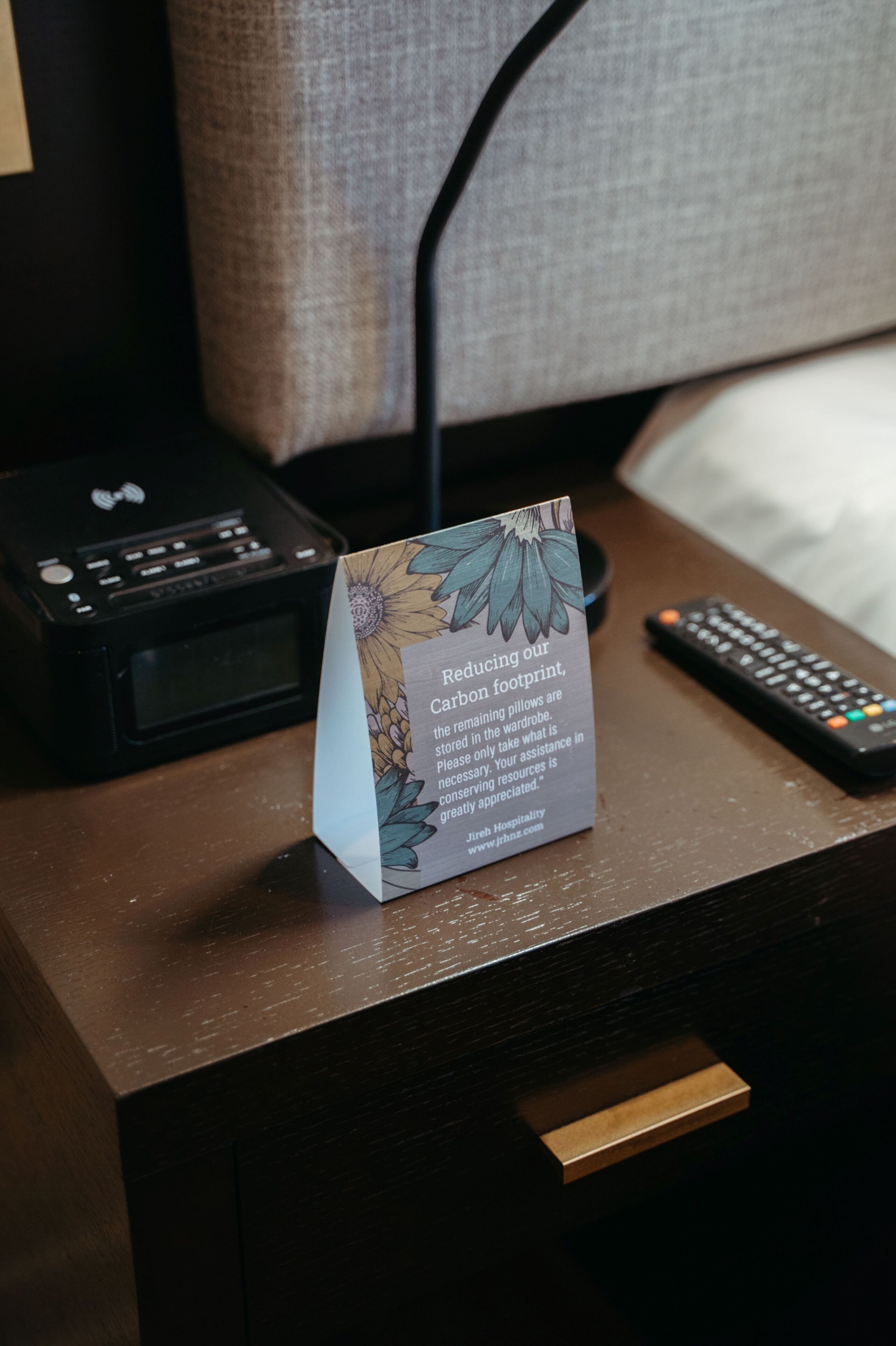 A hotel desk with a sign about reducing carbon footprint, a remote control, and a printer.