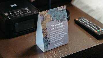 A hotel desk with a sign about reducing carbon footprint, a remote control, and a printer.