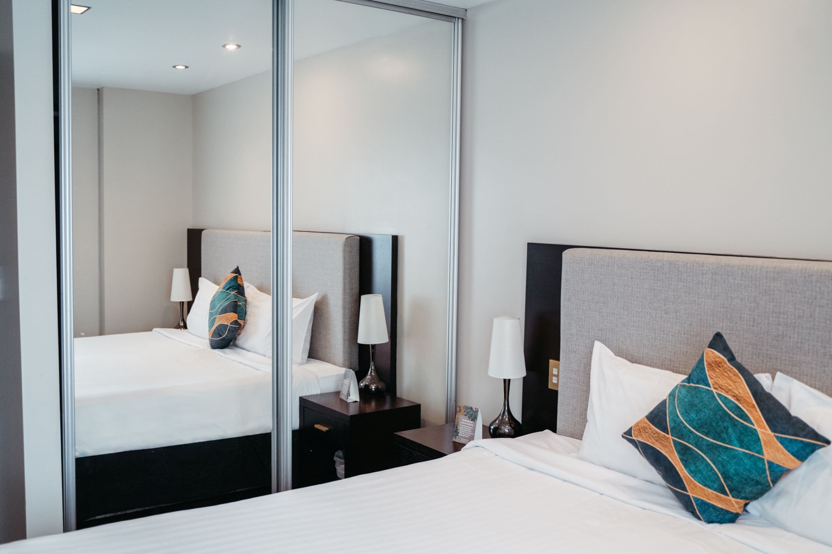Une chambre d’hôtel avec deux lits, un grand miroir et des tables de chevet avec des lampes.
