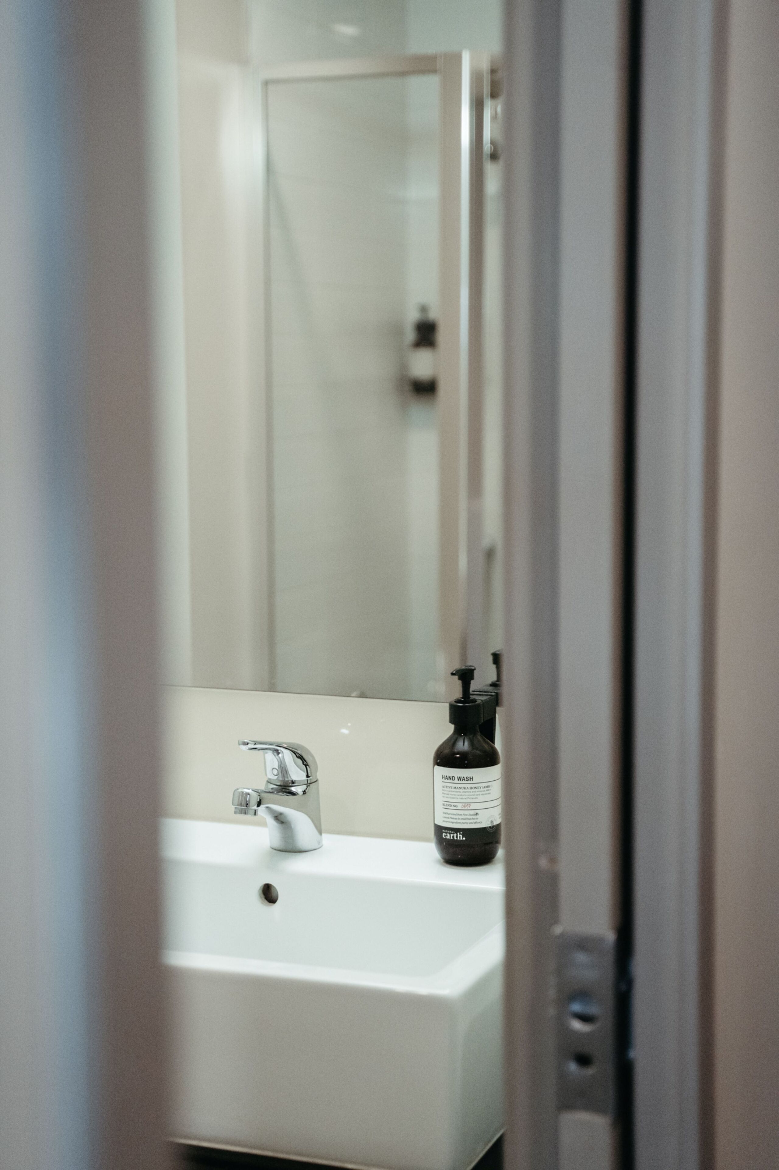 A bathroom with a white sink, a mirror, and a bottle of hand soap.
