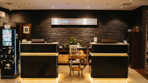 A reception area with a stone wall, a digital display, and a kiosk. - Auckland City Hotel (Auckland)
