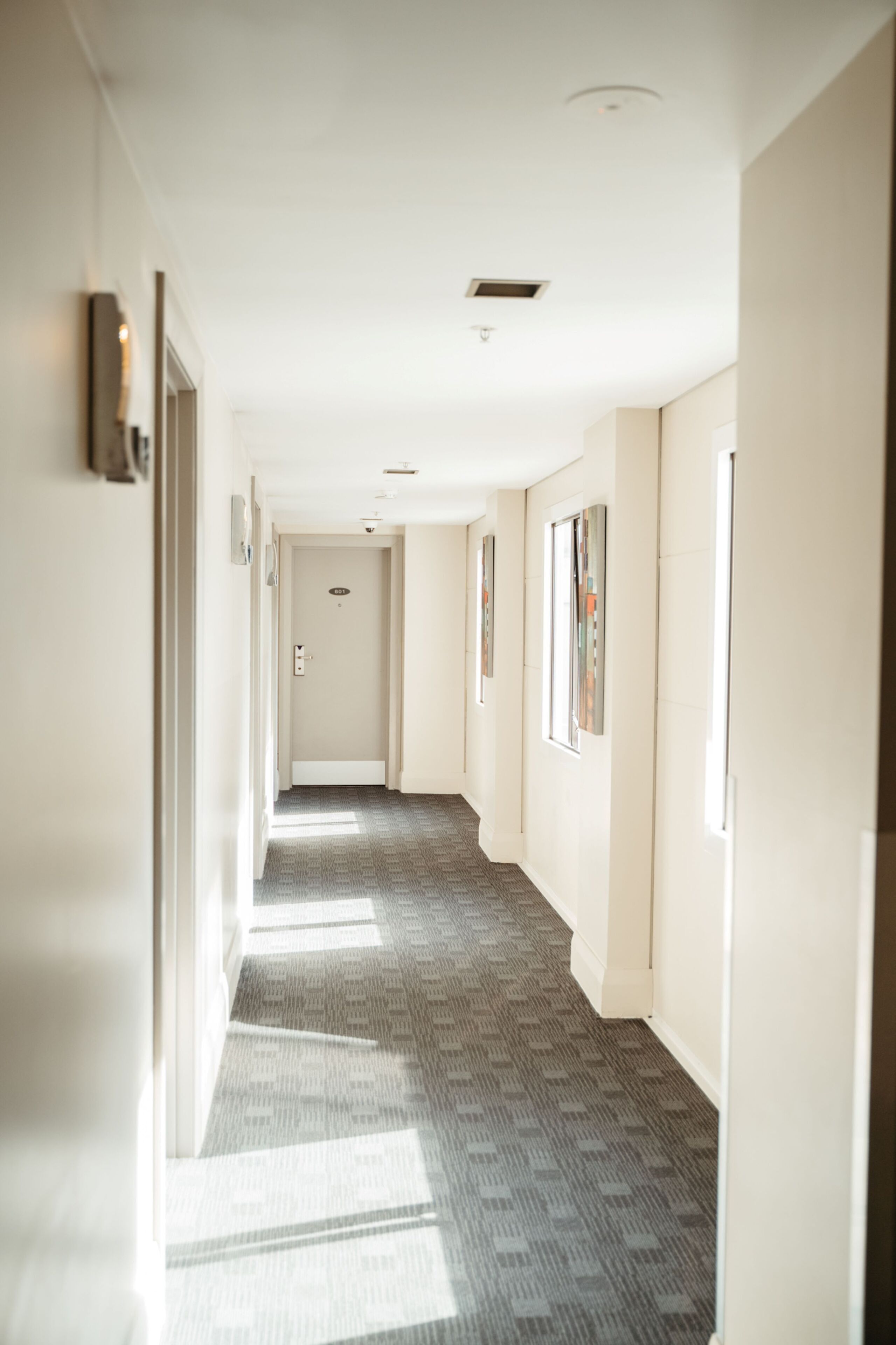 A long, narrow hallway with a patterned carpet, white walls, and a door at the end.