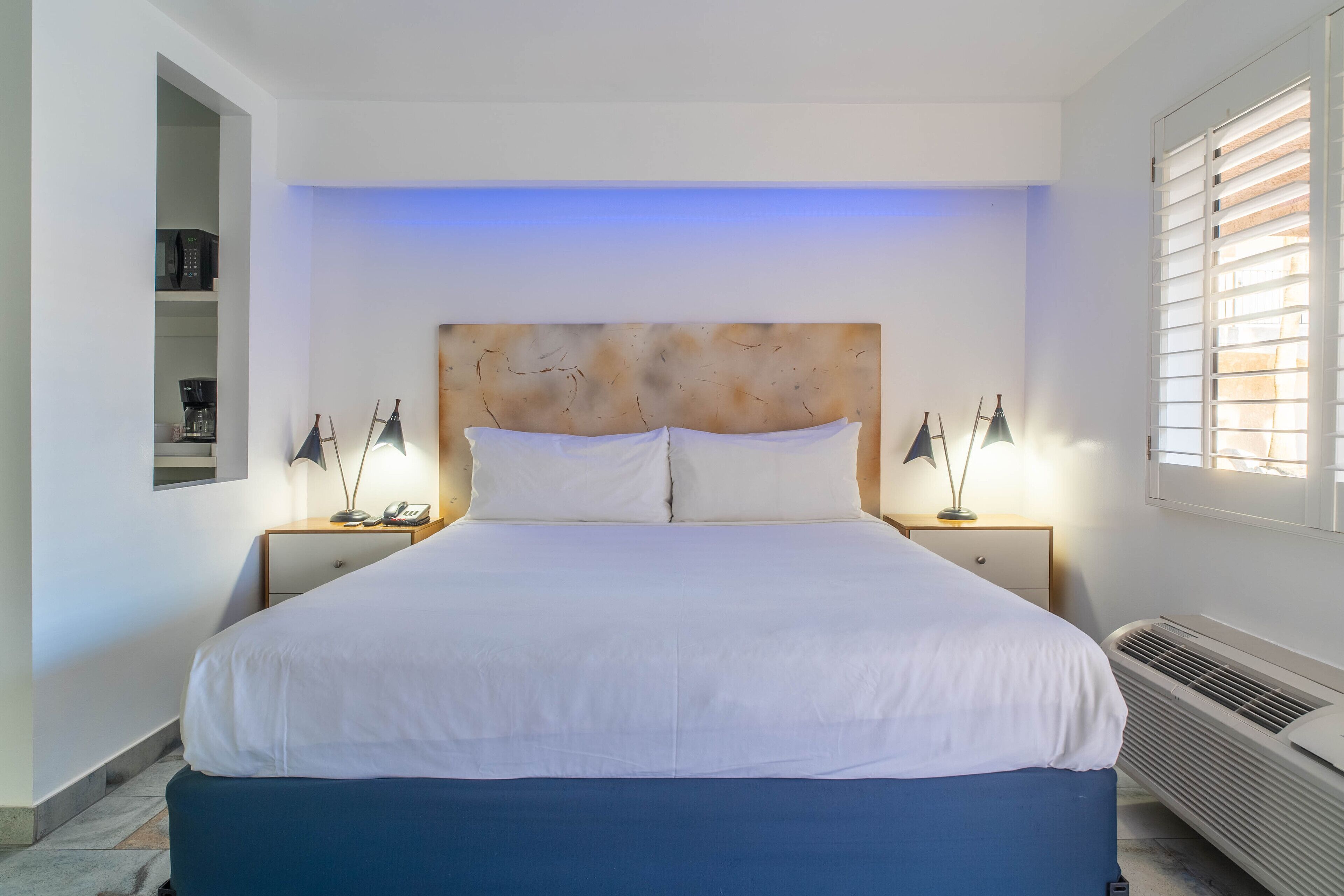 Un lit bien fait, avec du linge de lit blanc, une tête de lit en bois et deux tables de chevet avec des lampes.