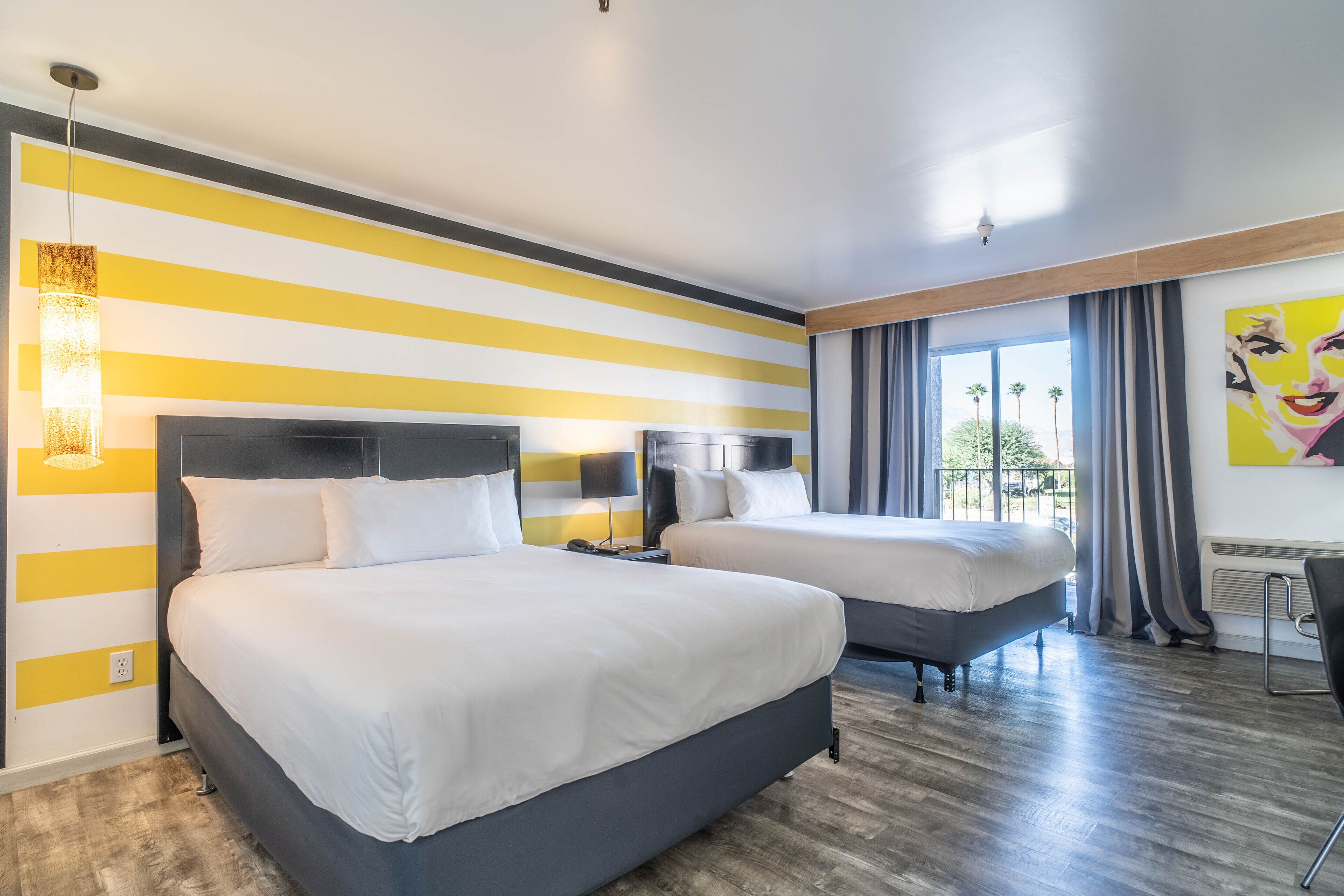 Habitación de hotel con dos camas, un ventanal con cortinas, un cuadro en la pared y una lámpara moderna.