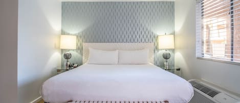A neatly arranged bedroom with a large bed, two bedside tables with lamps, a bench, and a wall-mounted air conditioner.