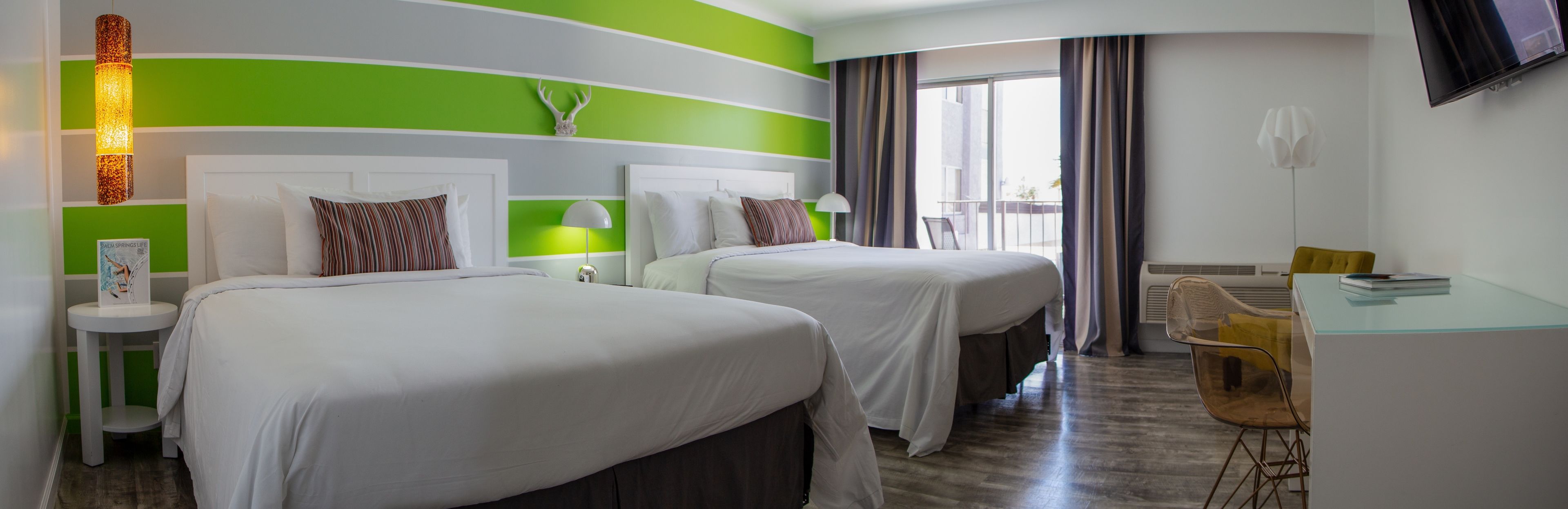A hotel room with two beds, a desk, and a TV.