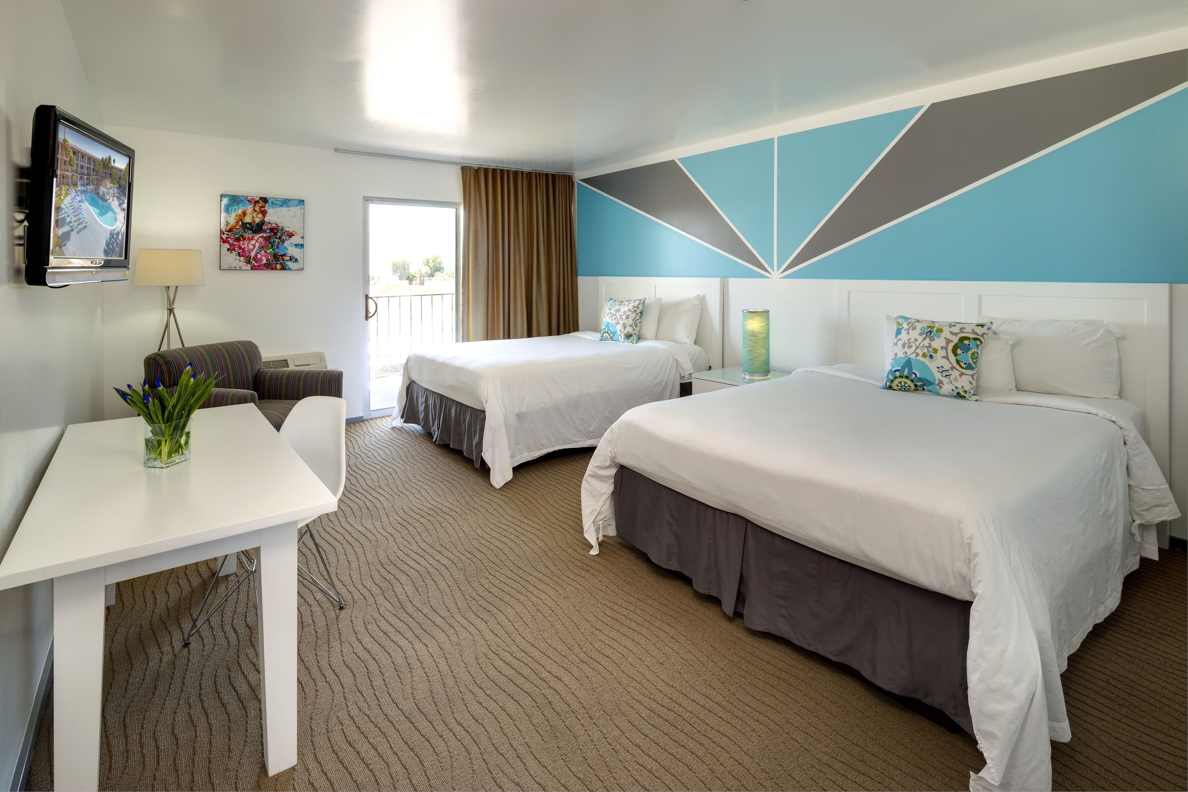 A hotel room with two beds, a desk, a TV, and a balcony with a view.