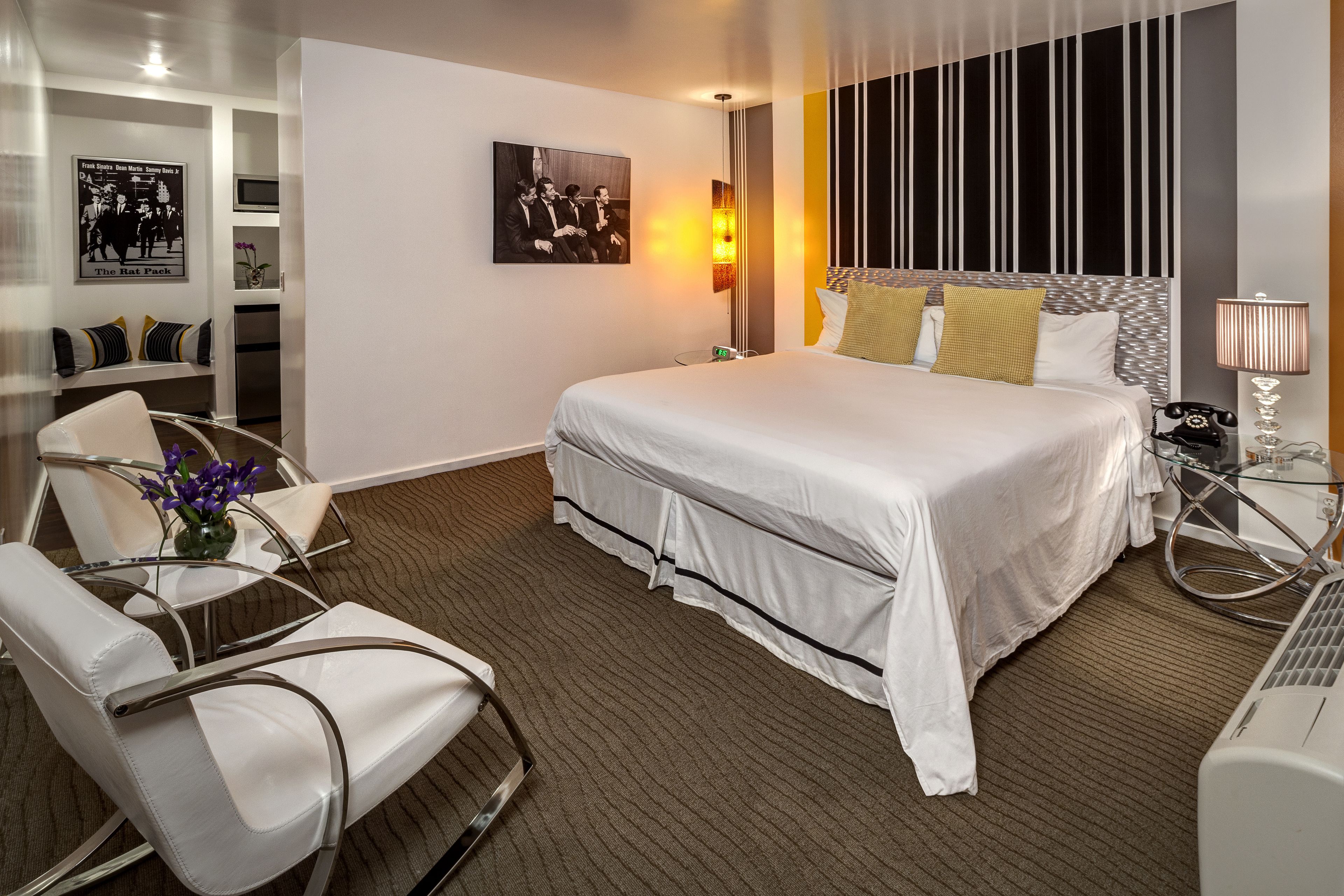 Une chambre d’hôtel avec un grand lit, un bureau avec une lampe, une chaise et une petite table sur laquelle est posé un vase de fleurs.