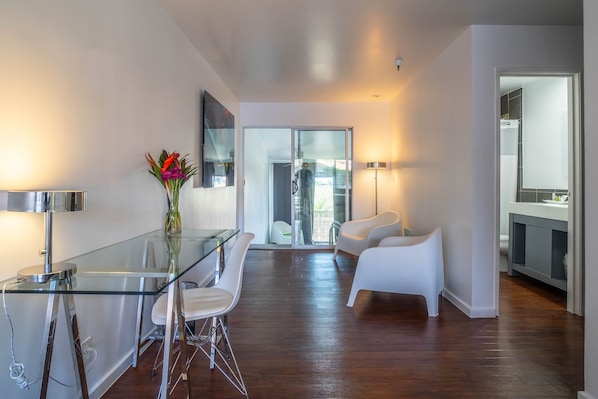 Un salon moderne avec une table à manger en verre, des chaises blanches, un vase rempli de fleurs et un grand miroir.