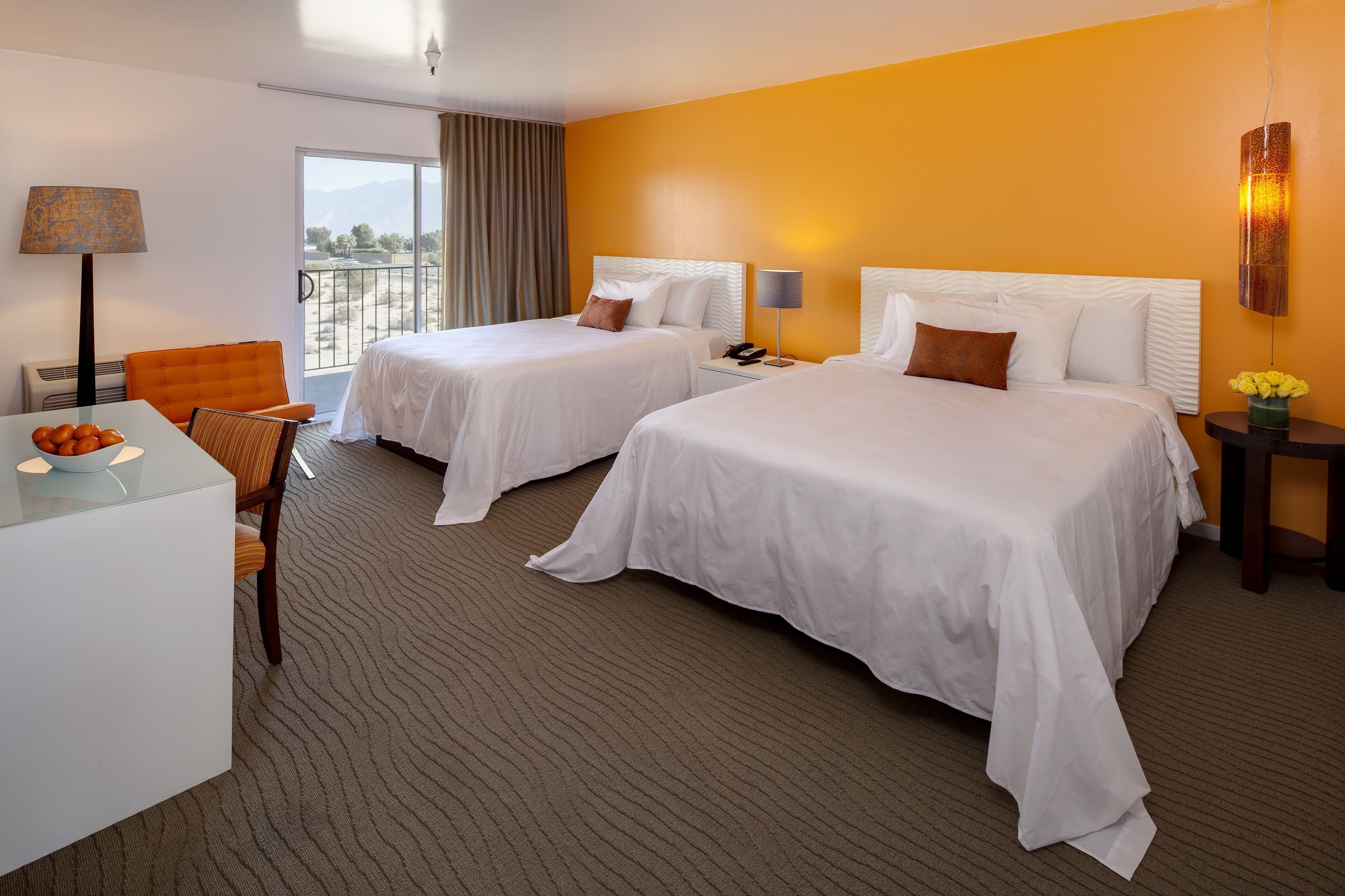 A hotel room with two beds, a desk, a chair, a lamp, and a nightstand with a phone.