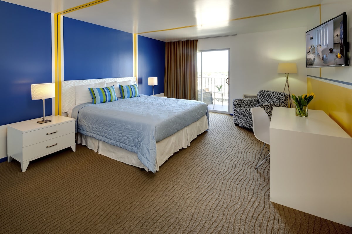 Ein Hotelzimmer mit Bett, Schreibtisch, Sessel, Fernseher und einem Balkon mit Blick.