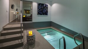 Een modern binnenzwembad met glazen wand, trap en decoratieve kandelaar.