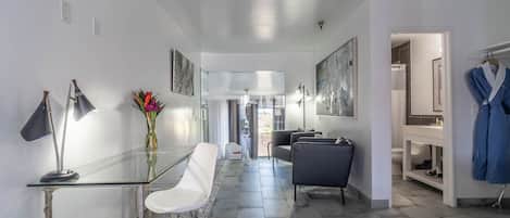 Un moderno vestíbulo de hotel con una mesa de vidrio, sillas blancas, un jarrón con flores y una bata azul colgada en la pared.