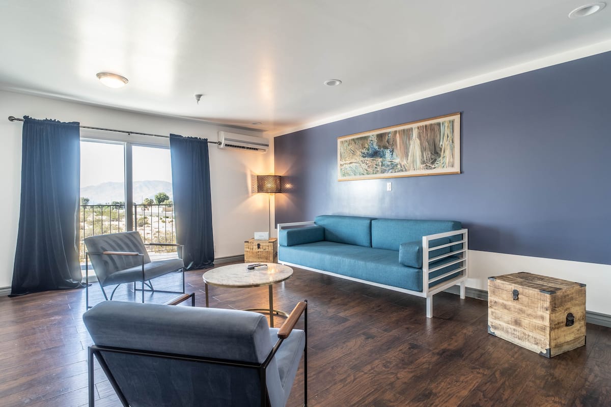 Ein modernes Wohnzimmer mit einem blauen Sofa, einem grauen Sessel, einem runden Couchtisch und einer Holzkommode.