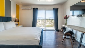 Een moderne hotelkamer met een groot bed, een bureau met twee stoelen, een televisie en een balkon met uitzicht op de bergen.