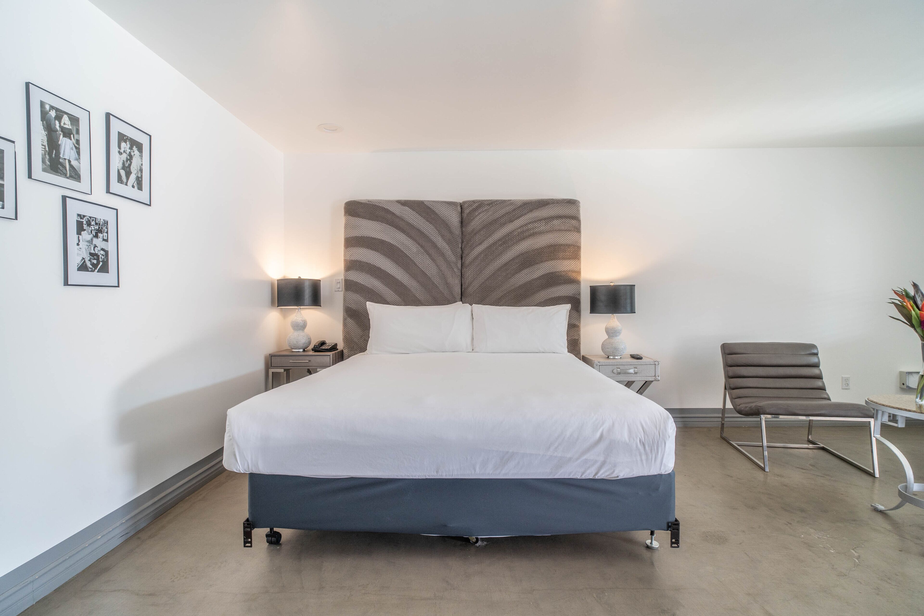 Ein modernes Hotelzimmer mit einem Bett, Nachttischlampen, einem Sessel und gerahmten Bildern an der Wand.
