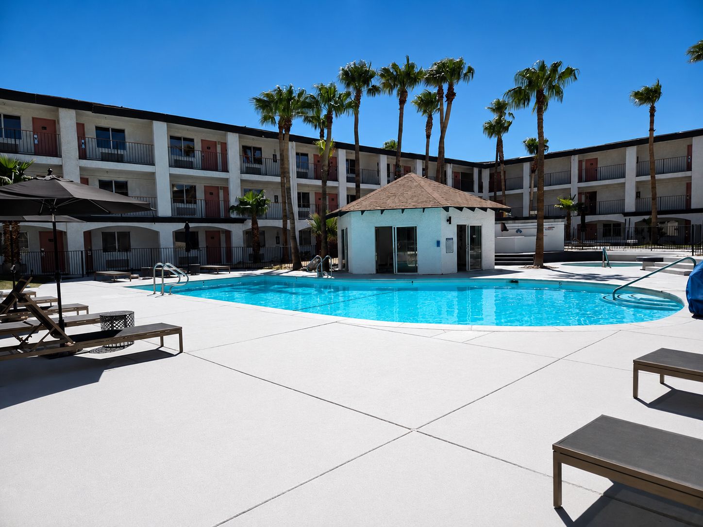 A pool area with lounge chairs, a small pool house, and palm trees.