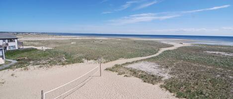 Ein Strand mit Volleyballnetz, einem Gebäude und blauem Himmel.