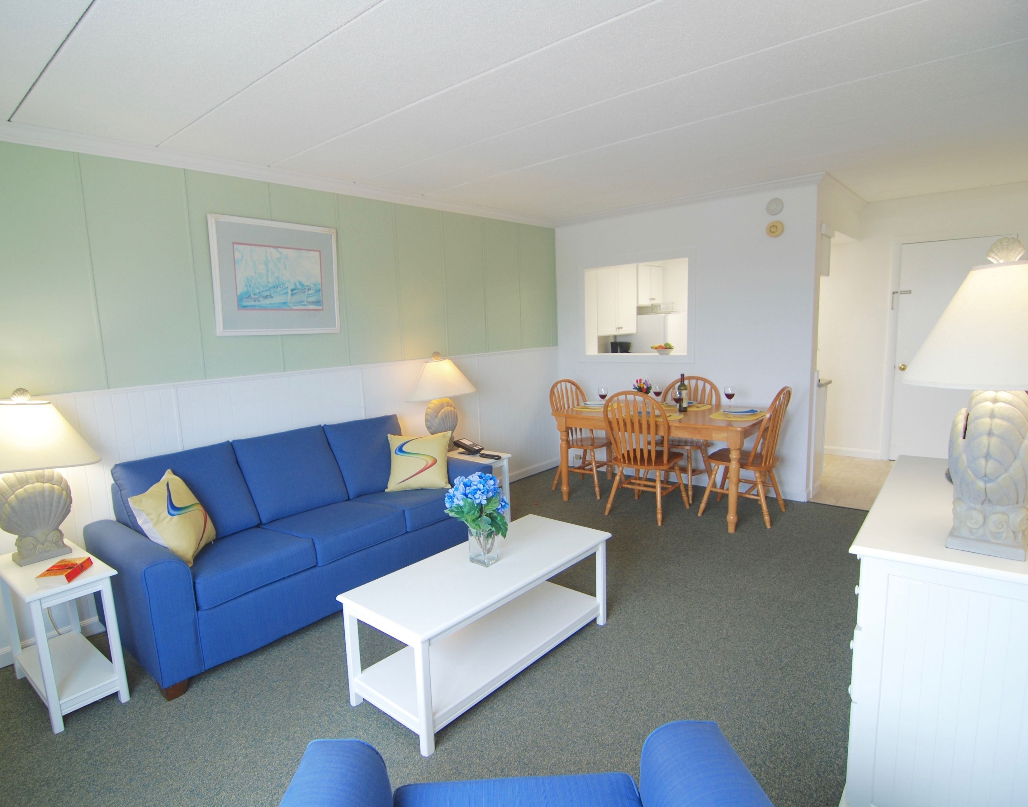 A living room with a blue sofa, a white coffee table, and a dining area with wooden chairs and a table.