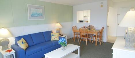 A living room with a blue sofa, a white coffee table, and a dining area with wooden chairs and a table.