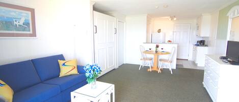 A living room with a blue sofa, a small white table with a vase, and a dining area with a white table and chairs.