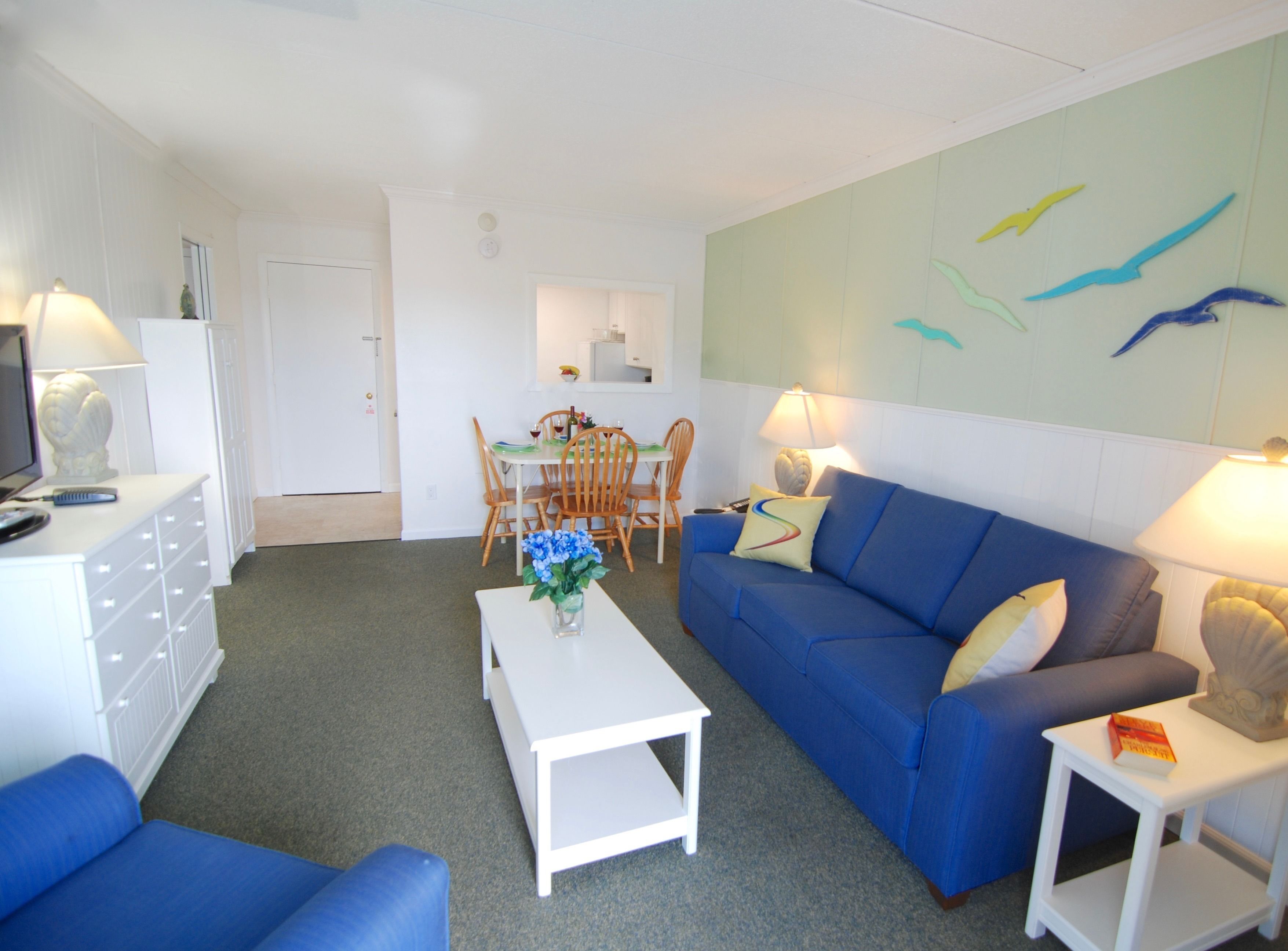 A living room with a blue sofa, white coffee table, and a dining area with wooden chairs and a table.