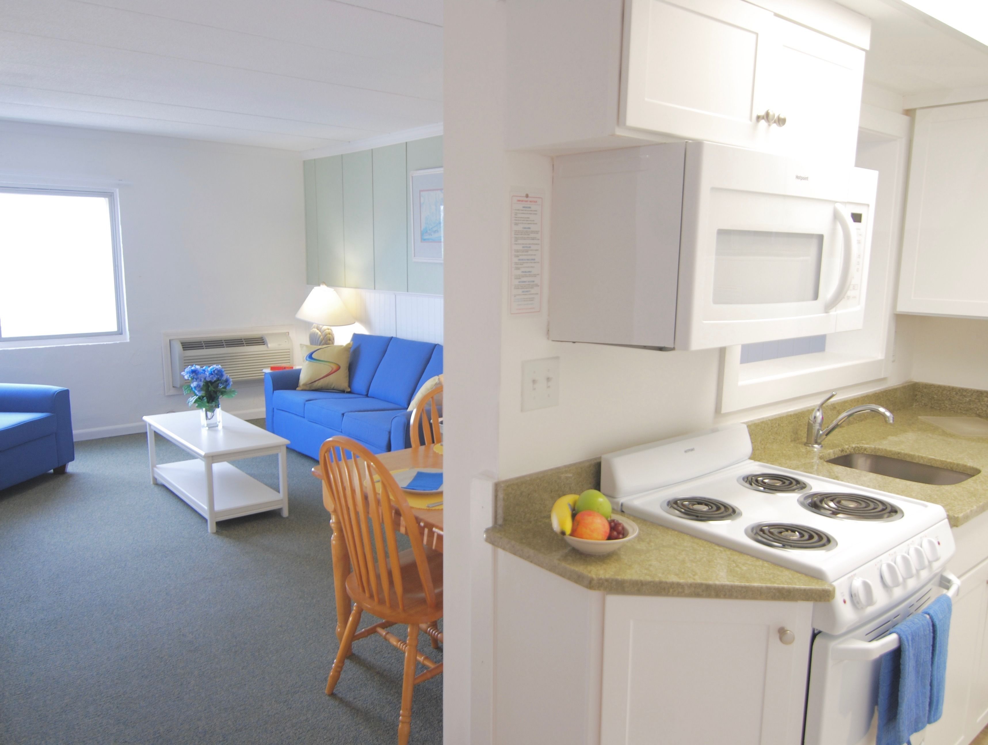 A compact kitchen with a stove, microwave, and sink. There's a dining area with a blue sofa and a small table.