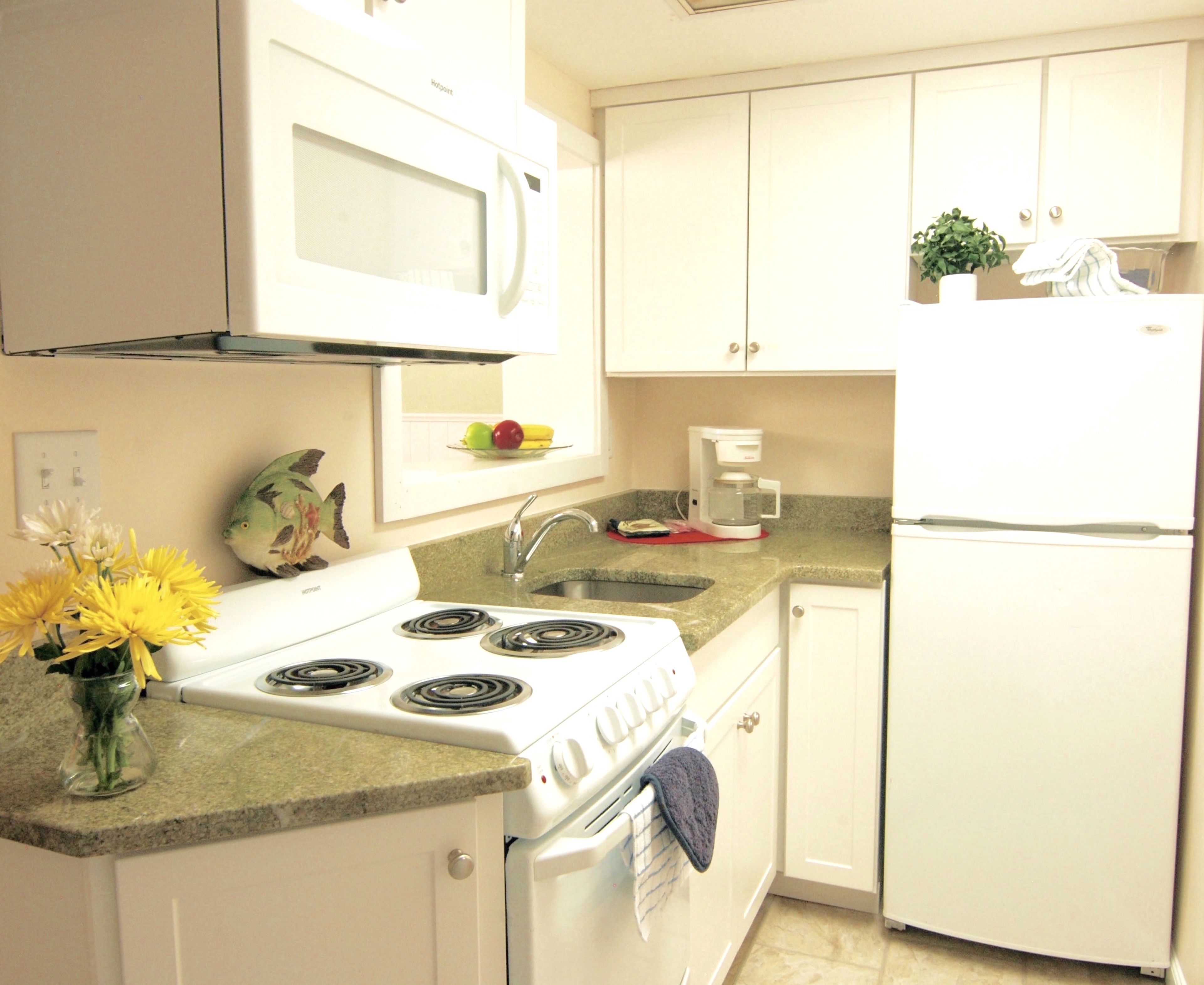 A kitchen with white cabinets, a stove, a microwave, a coffee maker, and a refrigerator.