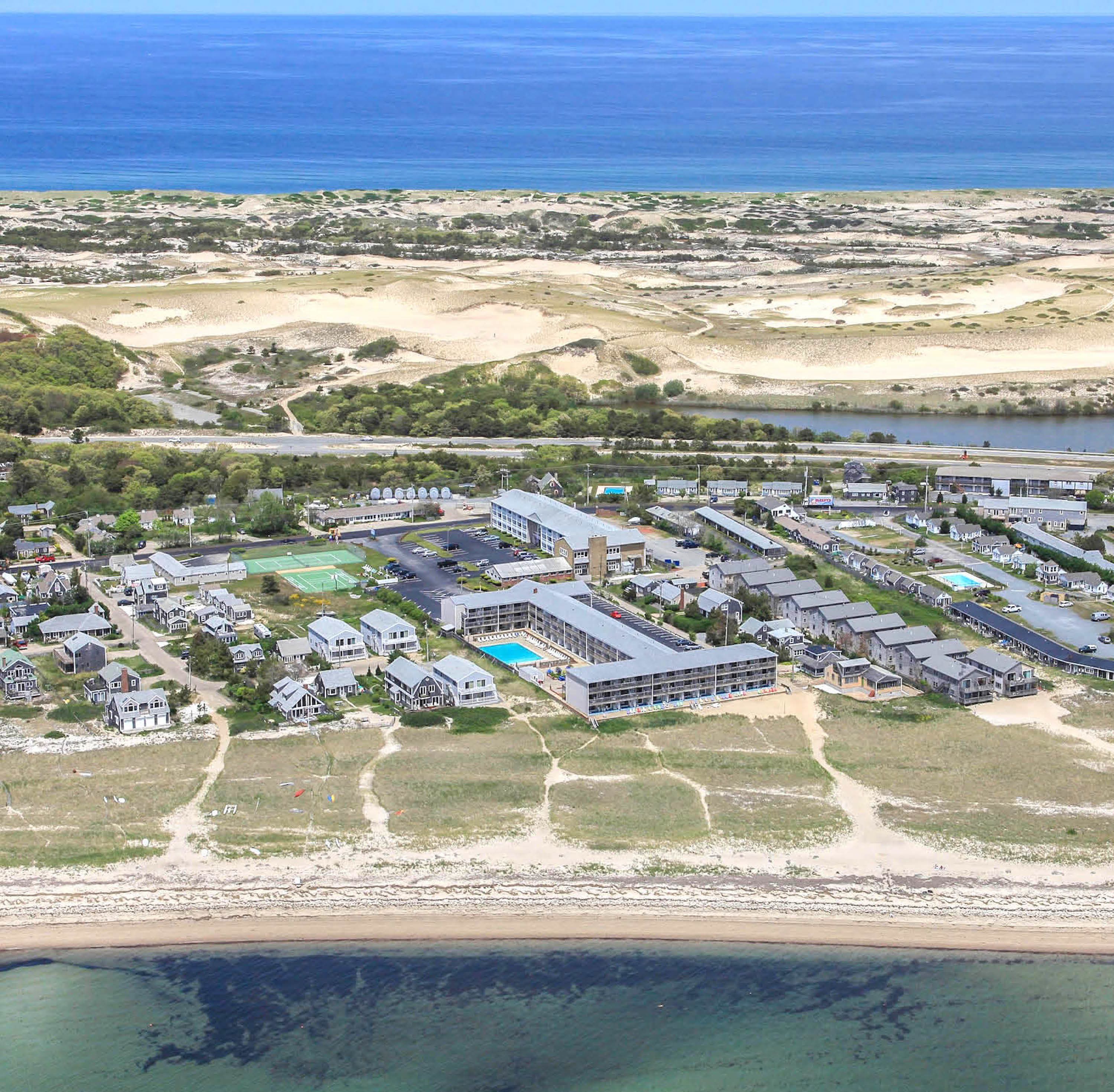 Ein Luftbild eines Küstenresorts mit mehreren Gebäuden, einem Schwimmbad und einem Strand.