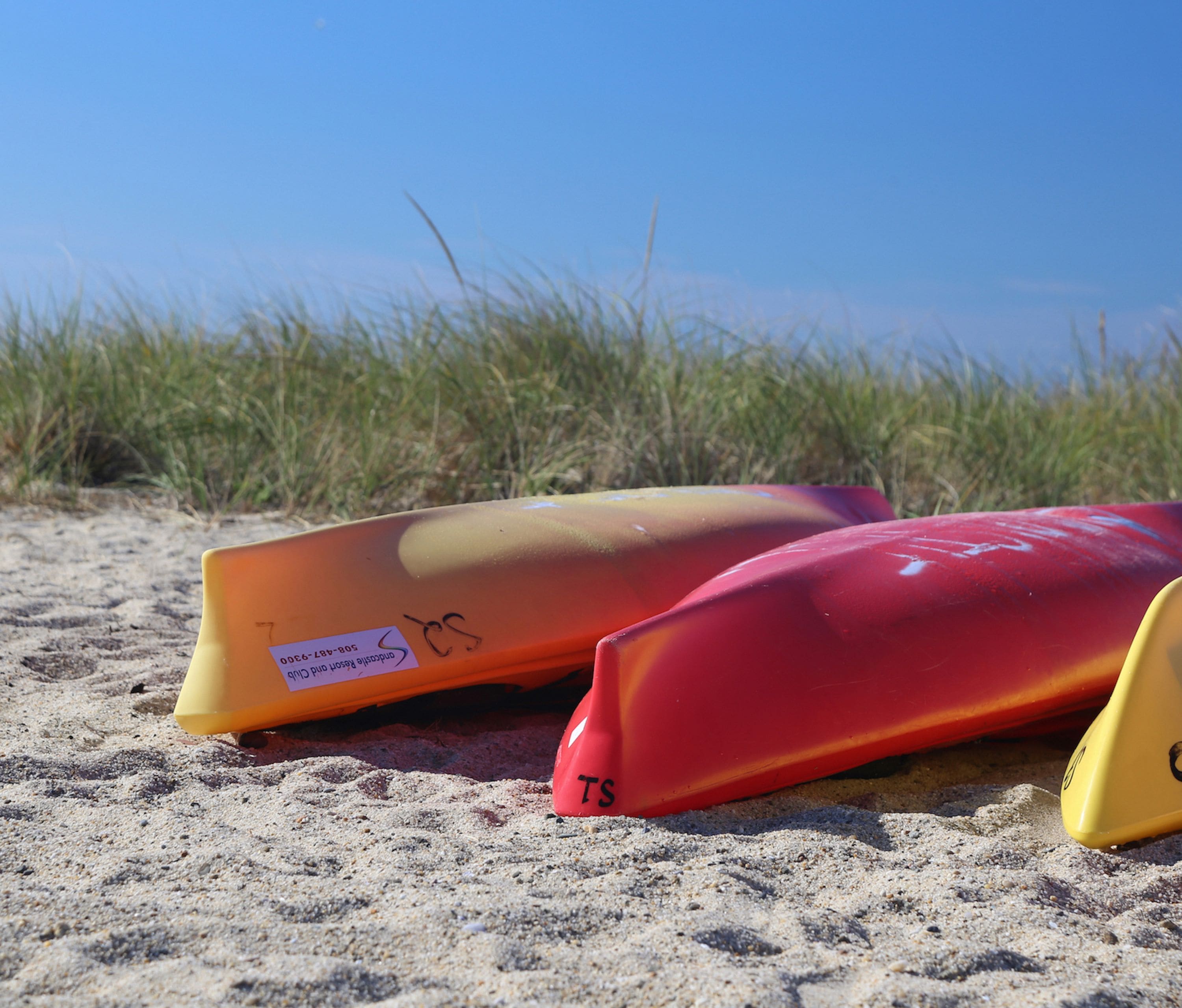 Two surfboards on a sandy beach with grass in the background.
